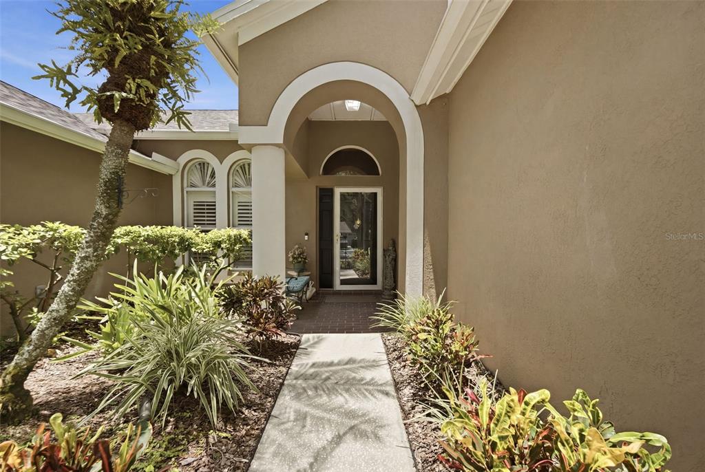 A concrete walkway leads to the covered front entrance of a tan stucco house — 10212 NEWINGTON PLACE, TAMPA, FL