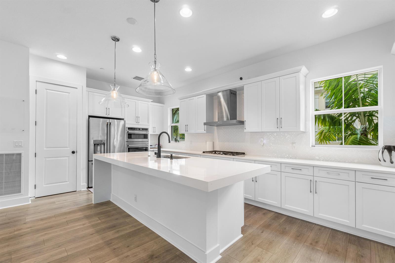 A modern white kitchen features a large quartz island, stainless steel appliances, and wood flooring — 12624 Machiavelli Way, Palm Beach Gardens FL 33418, PALM BEACH GARDENS, FL