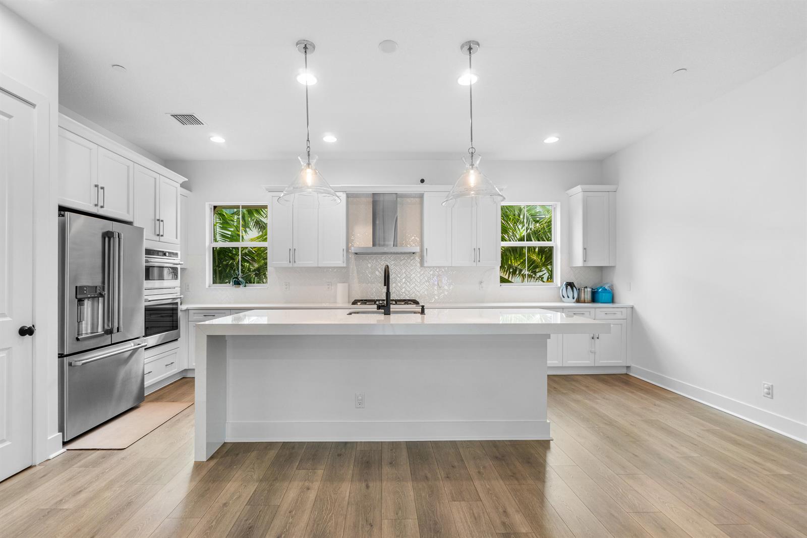 A modern white kitchen features a large island, stainless steel appliances, and light wood flooring — 12624 Machiavelli Way, Palm Beach Gardens FL 33418, PALM BEACH GARDENS, FL