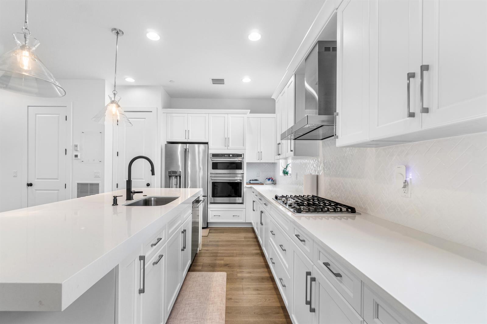 A modern white kitchen features a large island, stainless steel appliances, and wood-look flooring — 12624 Machiavelli Way, Palm Beach Gardens FL 33418, PALM BEACH GARDENS, FL