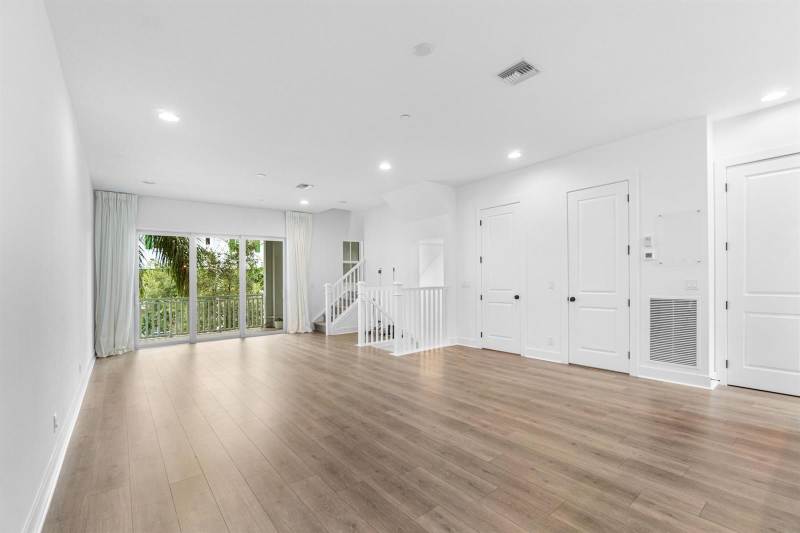 A bright, empty room features light wood flooring, white walls, and a staircase with railings — 12624 Machiavelli Way, Palm Beach Gardens FL 33418, PALM BEACH GARDENS, FL