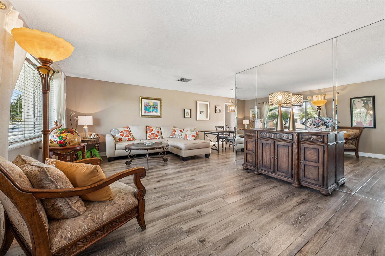 A living room features wood-look flooring, a sectional sofa, a wooden sideboard, and mirrored walls — 1702 SW 14th Avenue, Boynton Beach FL 33426, BOYNTON BEACH, FL