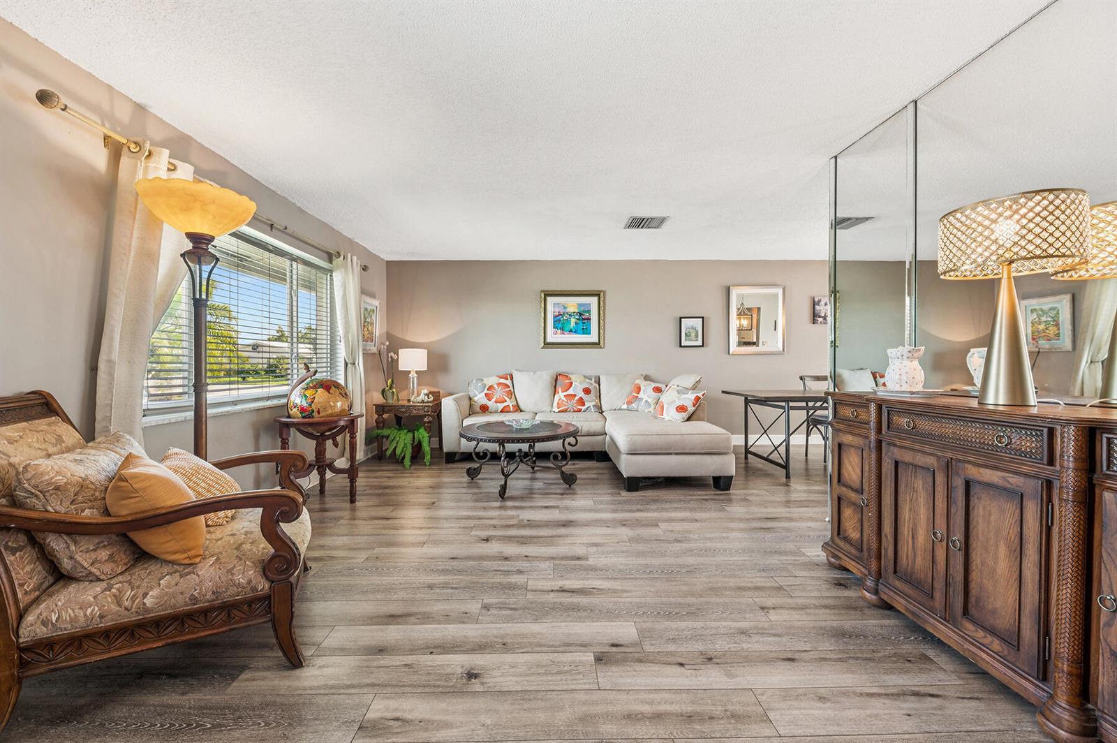 A living room features wood-look flooring, a sectional sofa, and a mirrored wall with a sideboard — 1702 SW 14th Avenue, Boynton Beach FL 33426, BOYNTON BEACH, FL