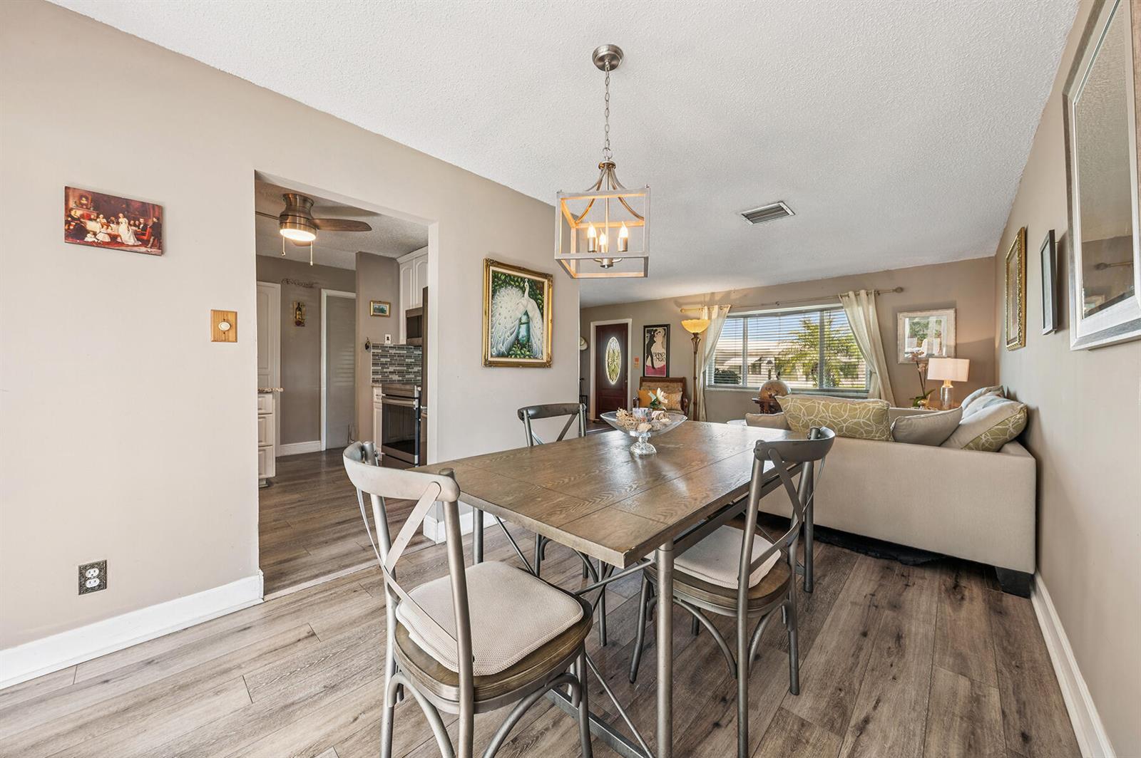 A dining area with a wooden table and chairs sits adjacent to a living room — 1702 SW 14th Avenue, Boynton Beach FL 33426, BOYNTON BEACH, FL