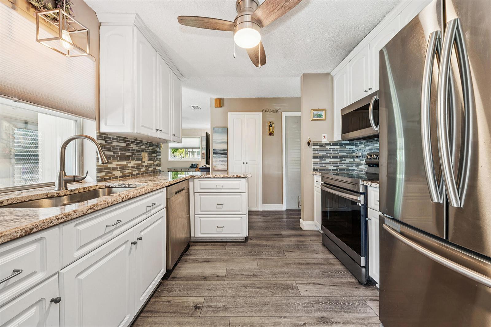 A kitchen features white cabinets, stainless steel appliances, granite countertops, and wood-look flooring — 1702 SW 14th Avenue, Boynton Beach FL 33426, BOYNTON BEACH, FL