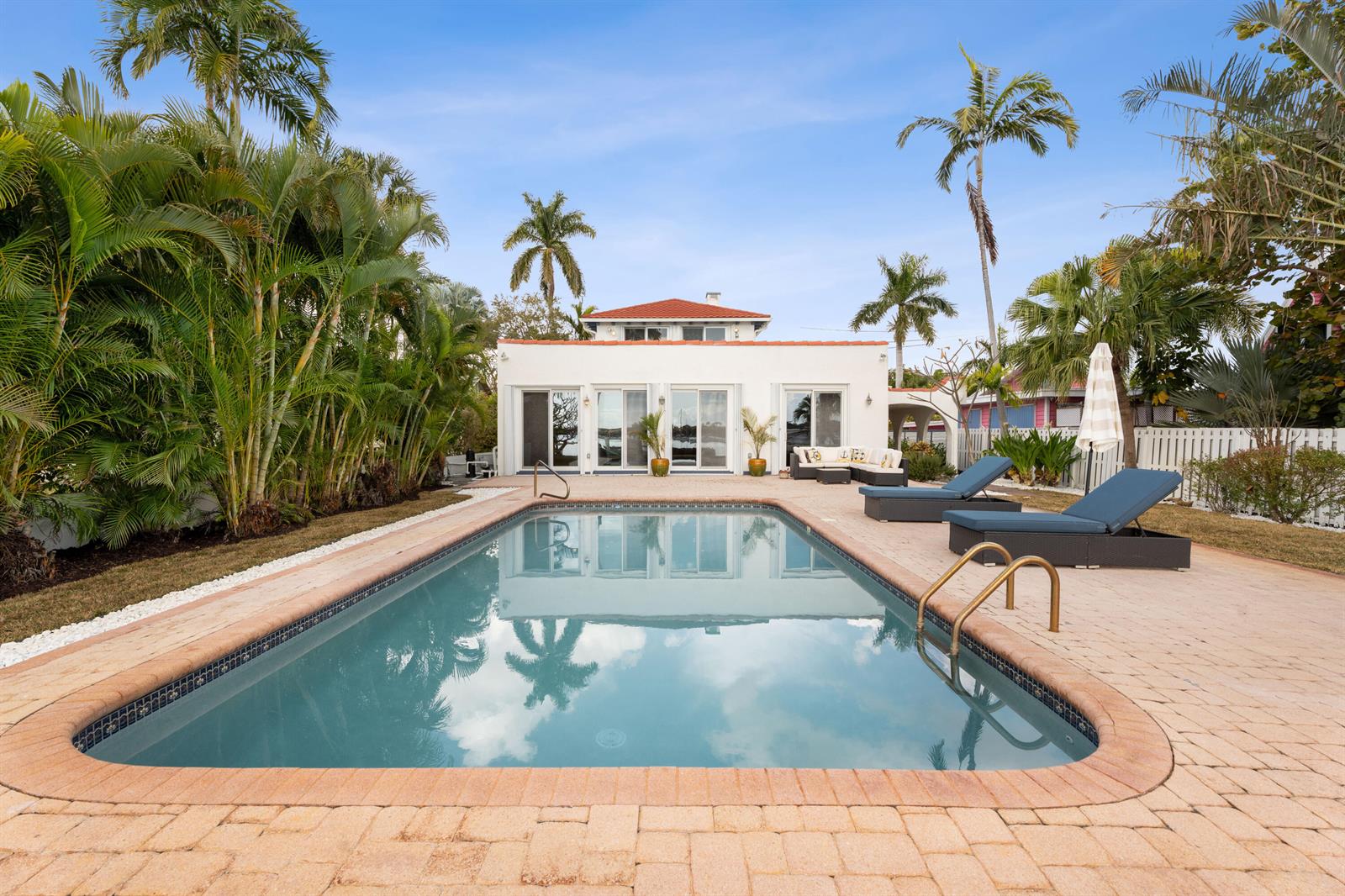 A rectangular swimming pool sits on a paved patio in front of a white house — 114 S Lake Drive, Lantana FL 33462, LANTANA, FL