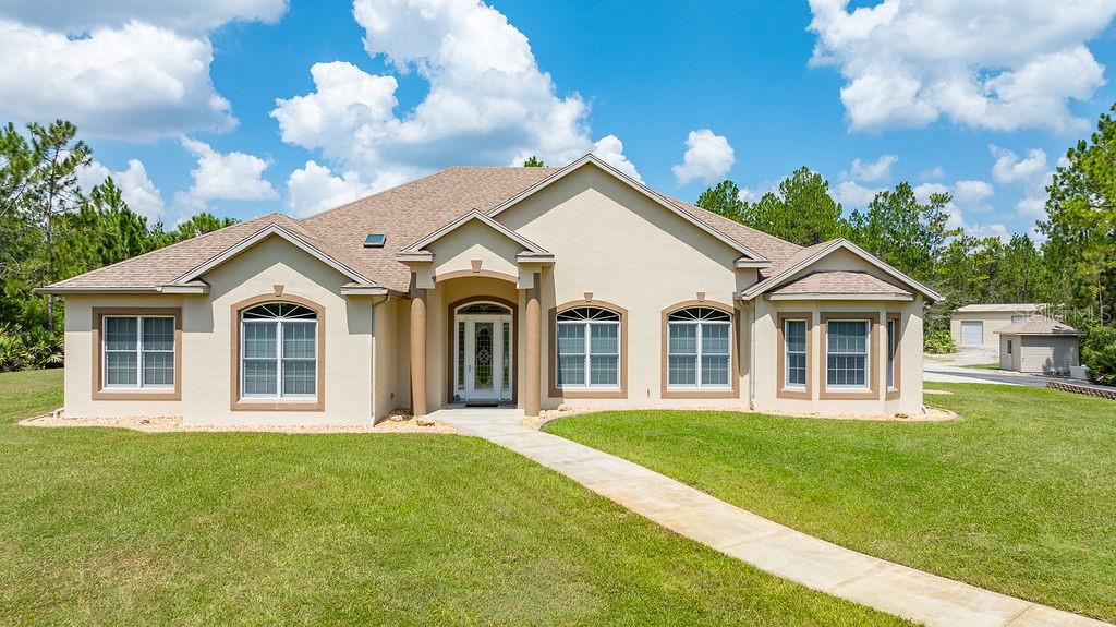 A single-story tan house with a front walkway, arched windows, and a detached garage — 147 ASHBY COVE LANE, NEW SMYRNA BEACH, FL