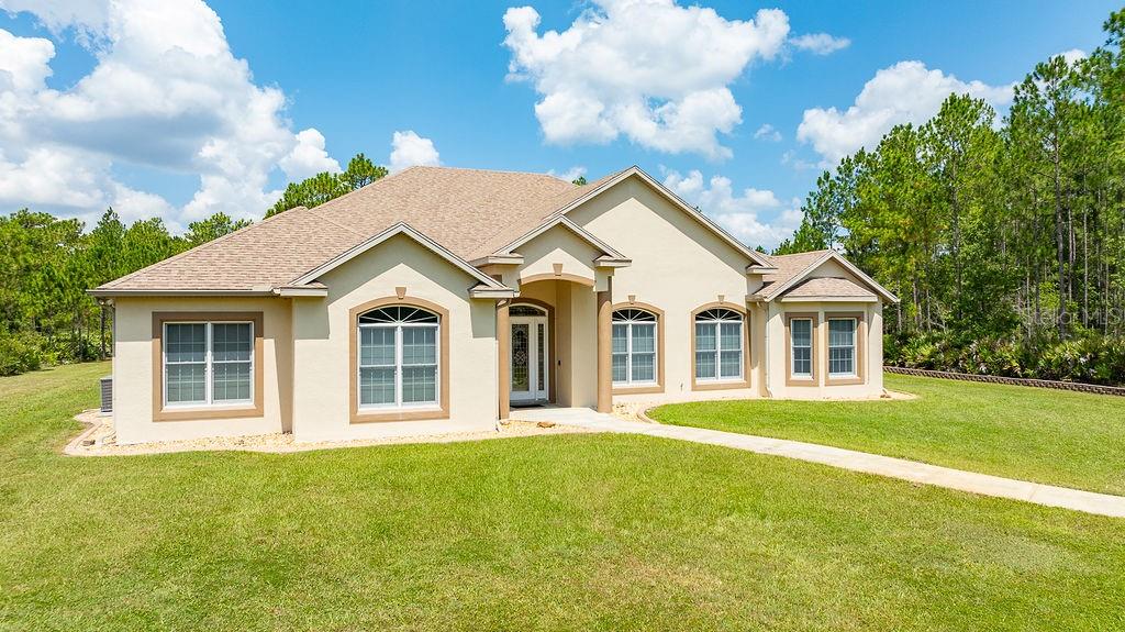 A single-story beige stucco house with a shingled roof sits on a grassy lot — 147 ASHBY COVE LANE, NEW SMYRNA BEACH, FL