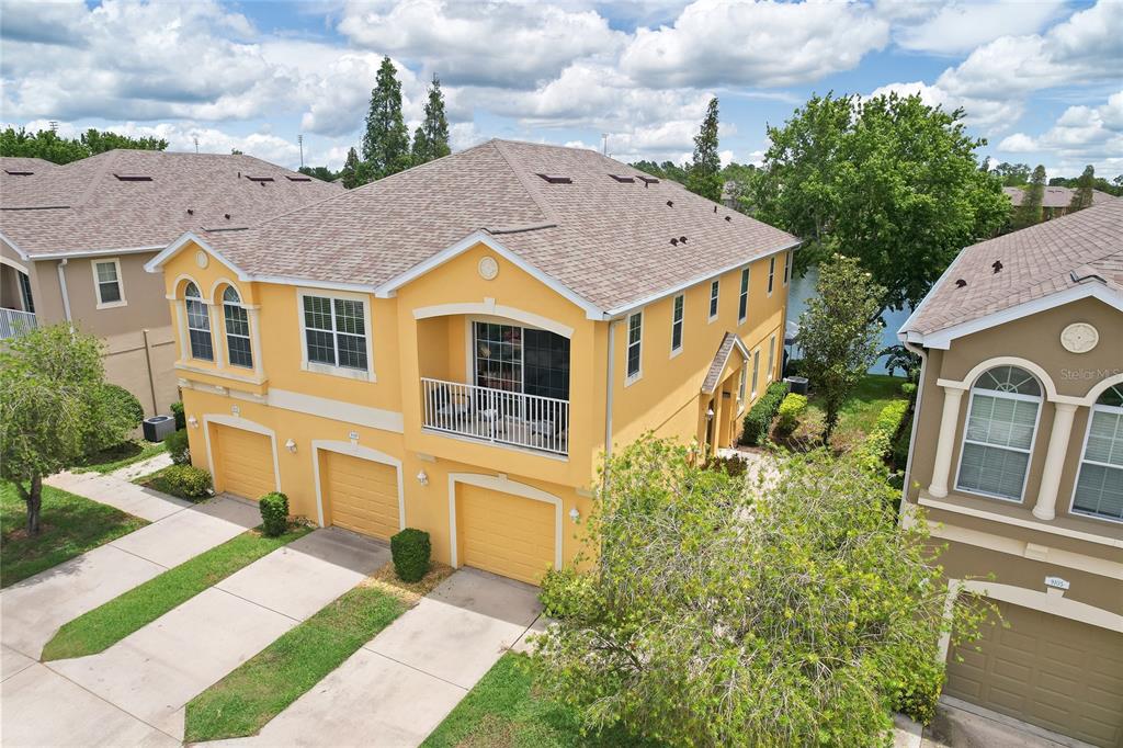 An aerial view shows a yellow two-story townhouse with a balcony and three garage doors — 9107 MOONLIT MEADOWS LOOP, RIVERVIEW, FL