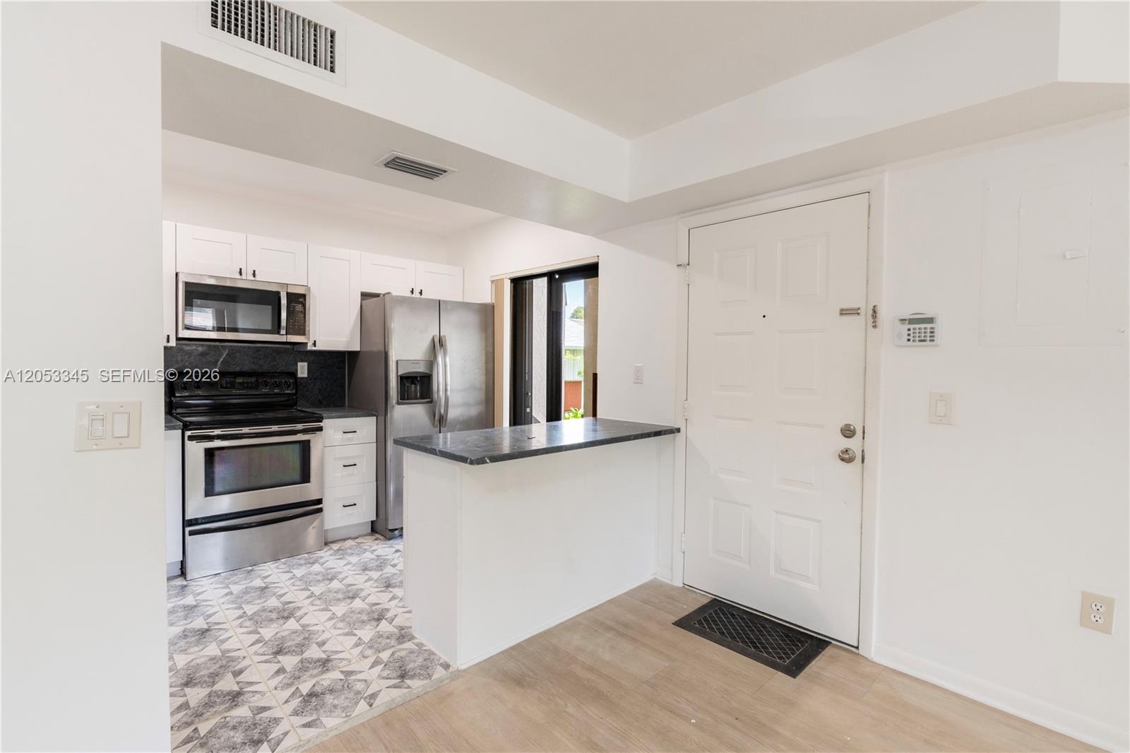 A kitchen features stainless steel appliances, white cabinetry, a breakfast bar, and patterned floor tiles — 20260 NE 3rd Ct # 2, Miami FL 33179, MIAMI, FL