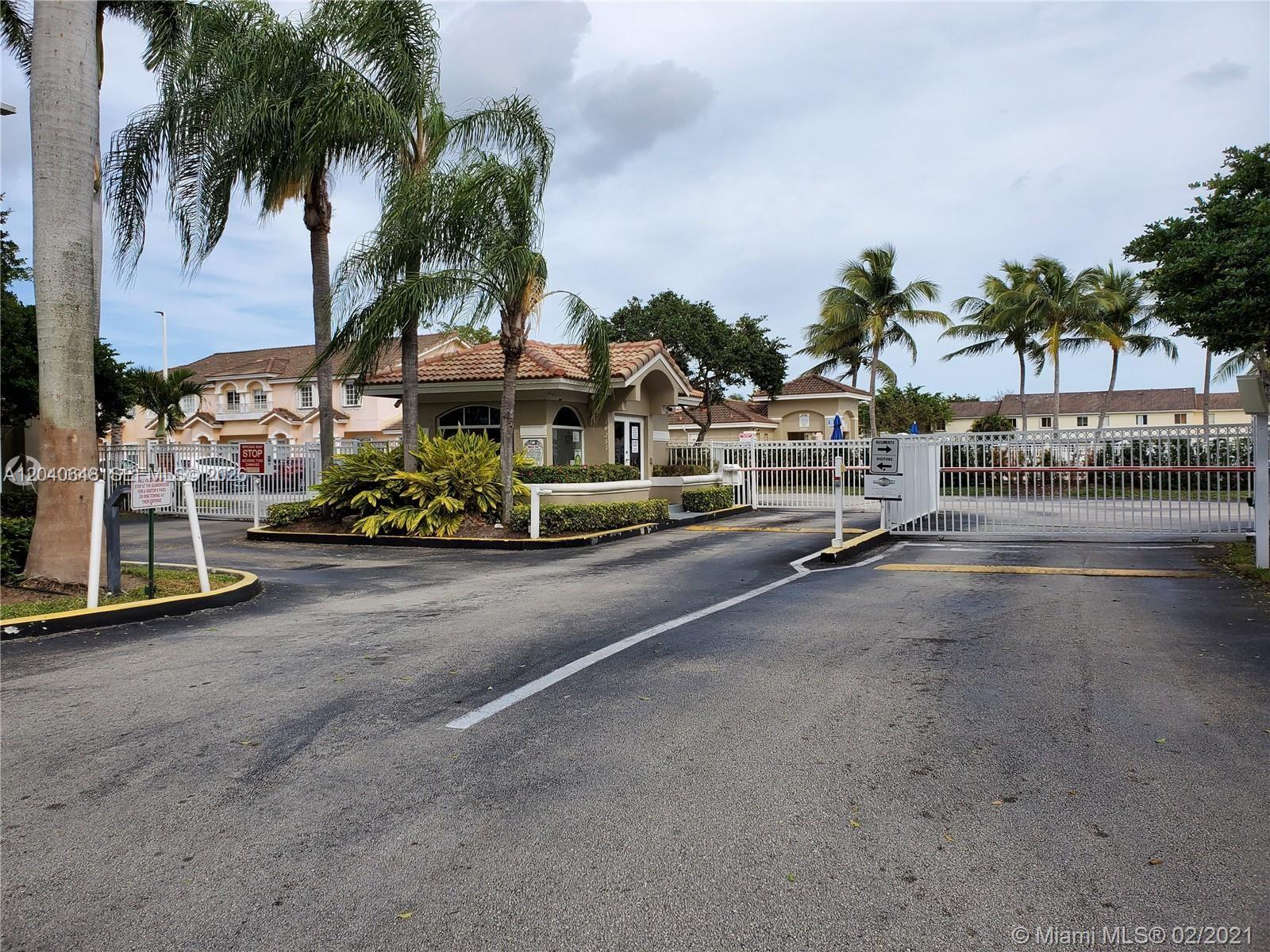 A gated entrance with a guardhouse, palm trees, and white metal fencing under a cloudy sky — 14169 SW 120th Ct # 13, Miami FL 33186, MIAMI, FL