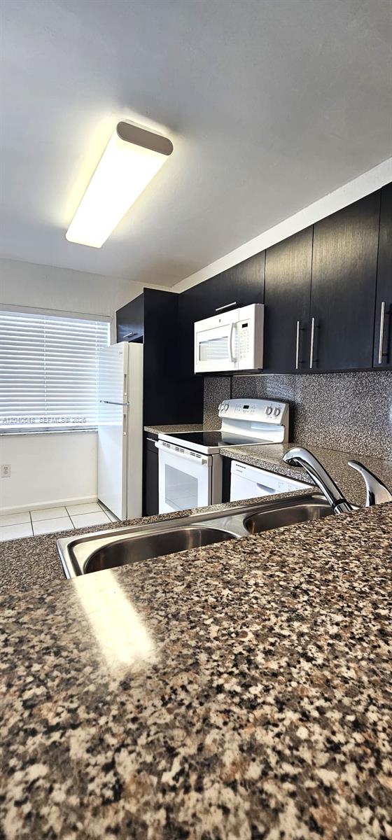 A kitchen features dark cabinets, granite countertops, a white refrigerator, and a stainless steel sink — 14169 SW 120th Ct # 13, Miami FL 33186, MIAMI, FL