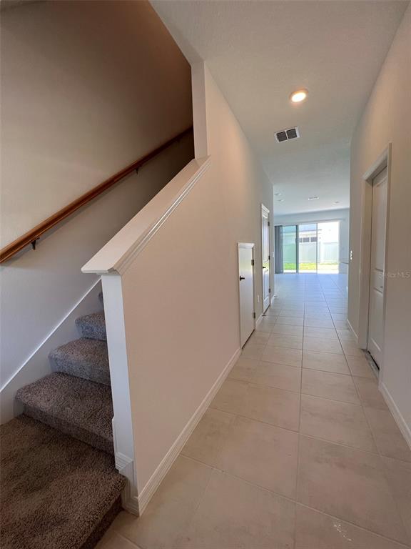A hallway with tiled floors leads toward a living area, with carpeted stairs on the left — 4553 TEOLI COURT, KISSIMMEE, FL