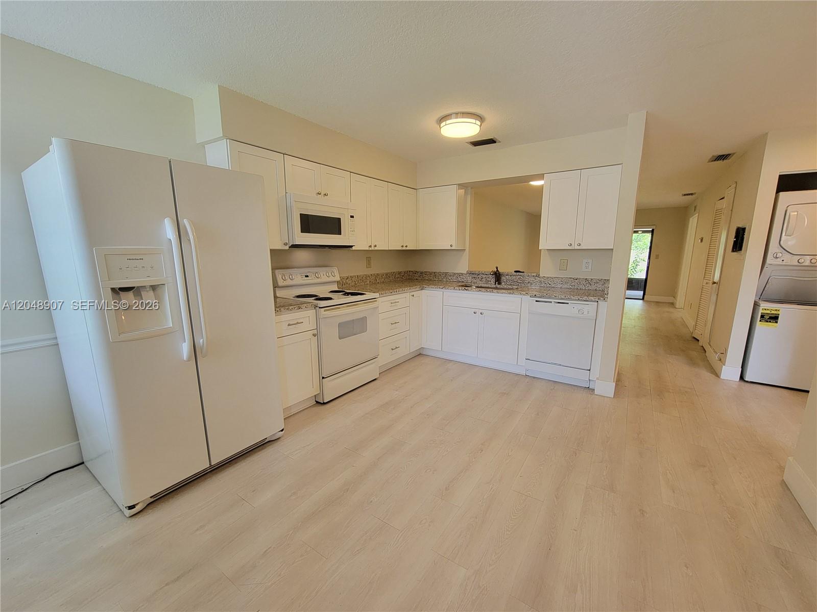 A white kitchen features granite countertops, white cabinetry, and light wood-look flooring — 6014 Indrio Rd # 3, Fort Pierce FL 34951, FORT PIERCE, FL
