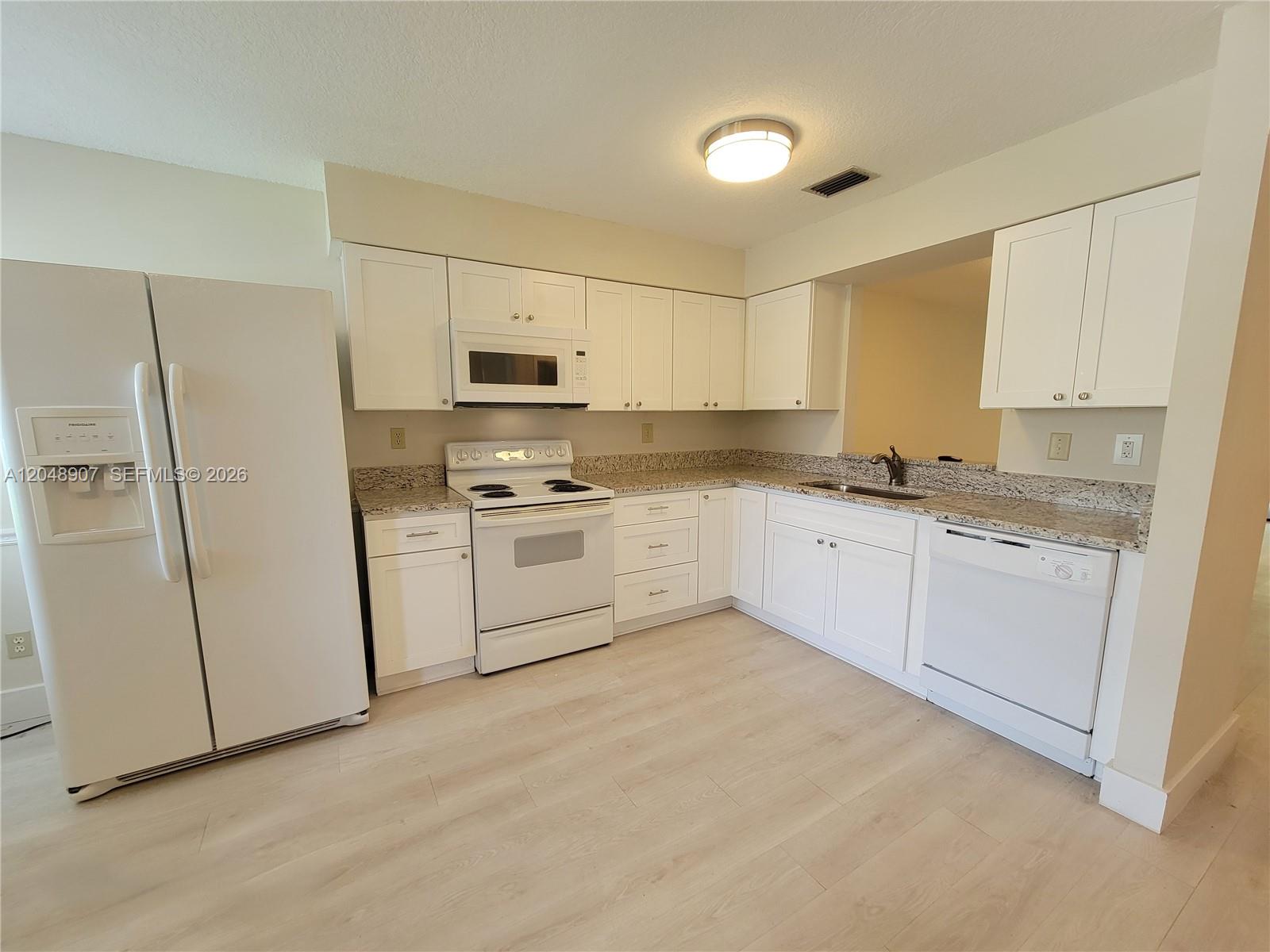 A kitchen features white cabinets, granite countertops, white appliances, and light wood-look flooring — 6014 Indrio Rd # 3, Fort Pierce FL 34951, FORT PIERCE, FL