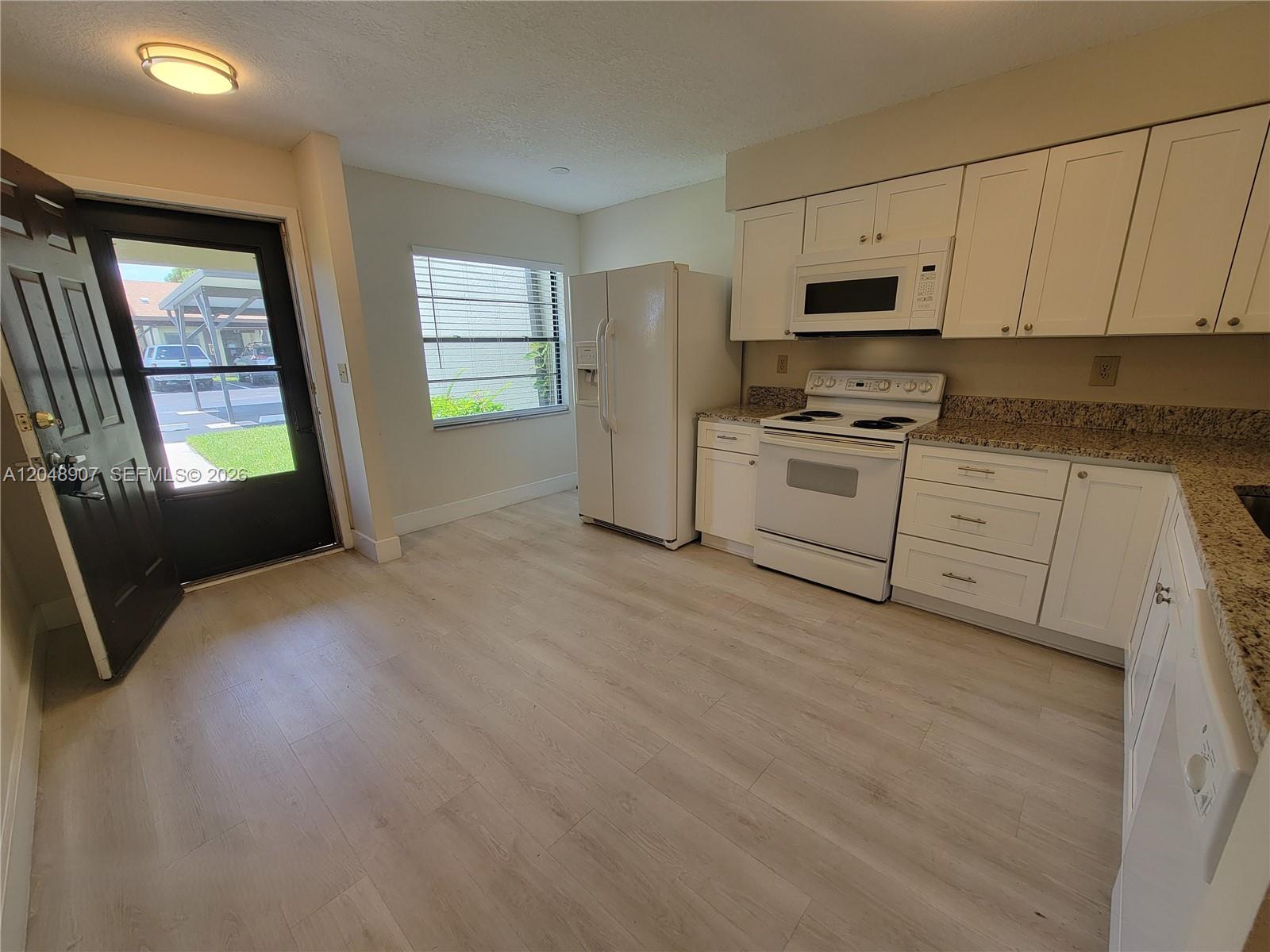 A kitchen features white cabinets, granite countertops, white appliances, and light wood-look flooring — 6014 Indrio Rd # 3, Fort Pierce FL 34951, FORT PIERCE, FL