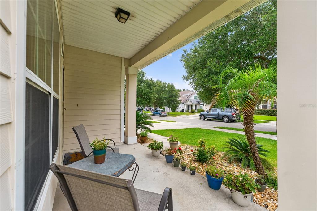A covered front porch features patio furniture and several potted plants overlooking a suburban street — 8206 NW 52ND STREET, GAINESVILLE, FL