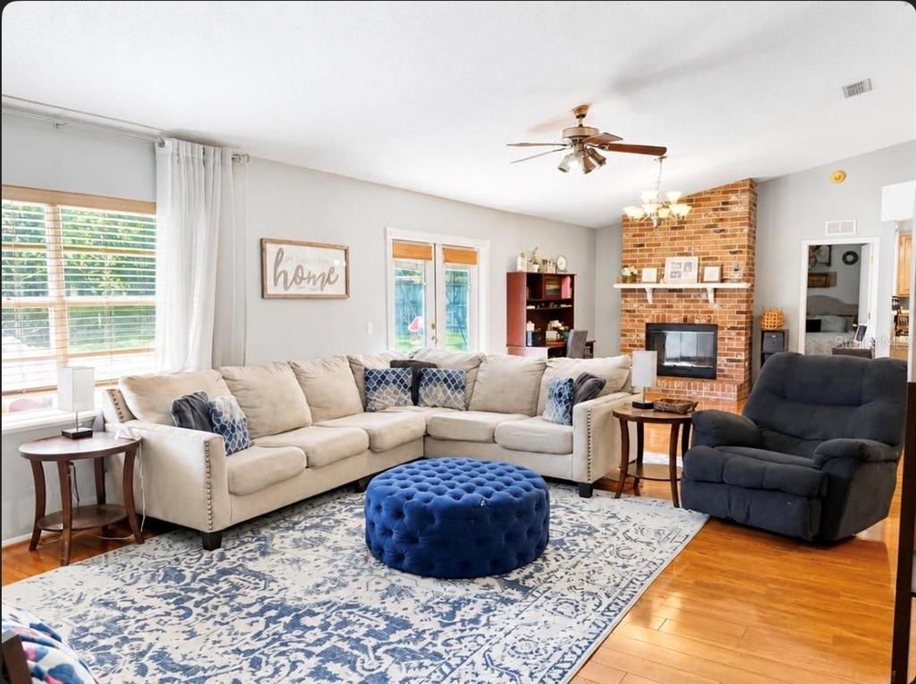 A living room features a beige sectional, blue tufted ottoman, and a brick fireplace — 561 ASTORIA DRIVE, DELAND, FL