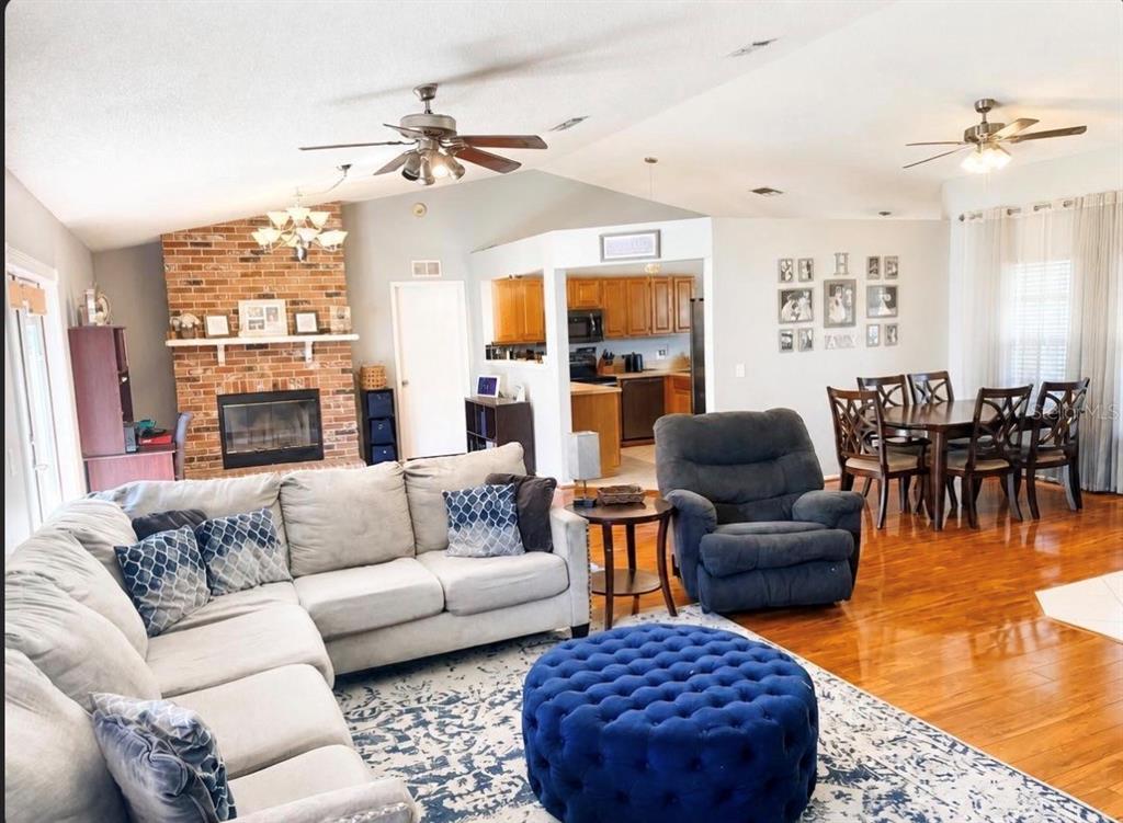 A living room with a brick fireplace, sectional sofa, blue ottoman, and adjacent dining area — 561 ASTORIA DRIVE, DELAND, FL