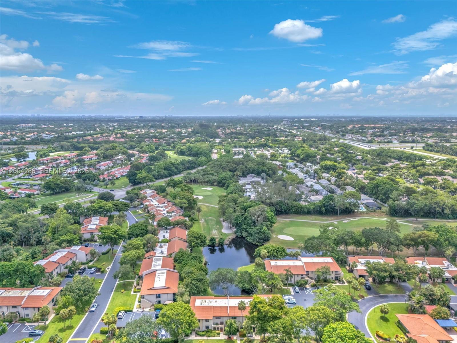An aerial view shows residential buildings with orange roofs surrounding a pond and golf course — 21698 Cypress Rd # 44D, Boca Raton FL 33433, BOCA RATON, FL