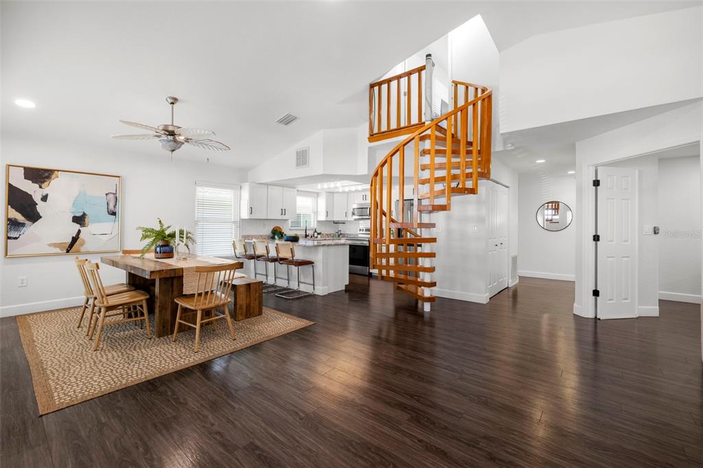 An open-concept dining area and kitchen feature a wooden spiral staircase and dark flooring — 247 126TH AVENUE, TREASURE ISLAND, FL