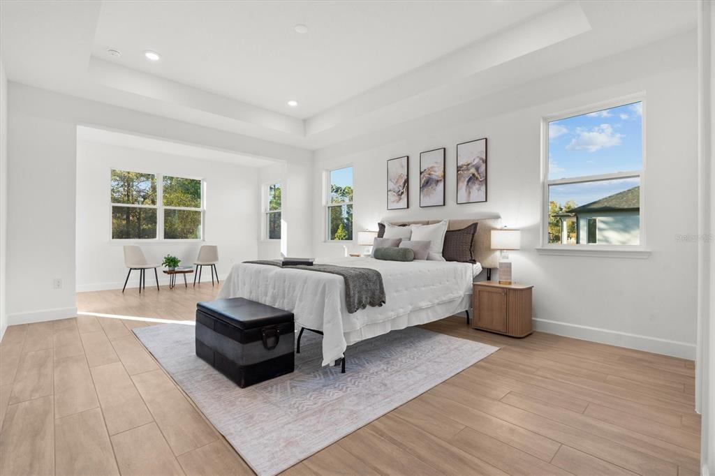 A spacious bedroom with light wood floors, a tray ceiling, and a seating area — 5204 BAKER AVENUE, ORLANDO, FL