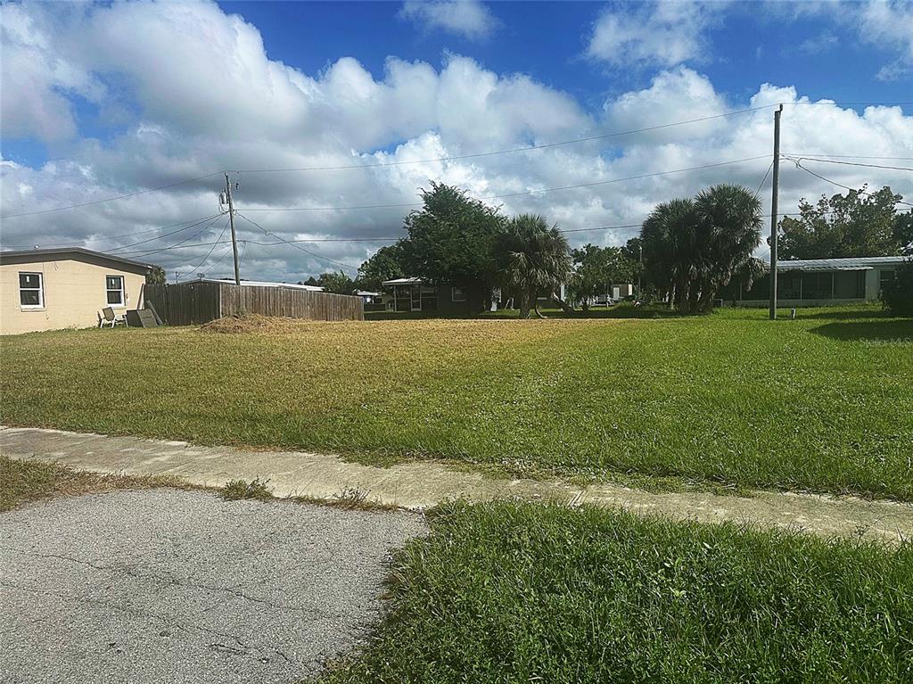 A vacant, grassy residential lot sits between two houses under a cloudy blue sky — 3420 CROTON TERRACE, PORT CHARLOTTE, FL