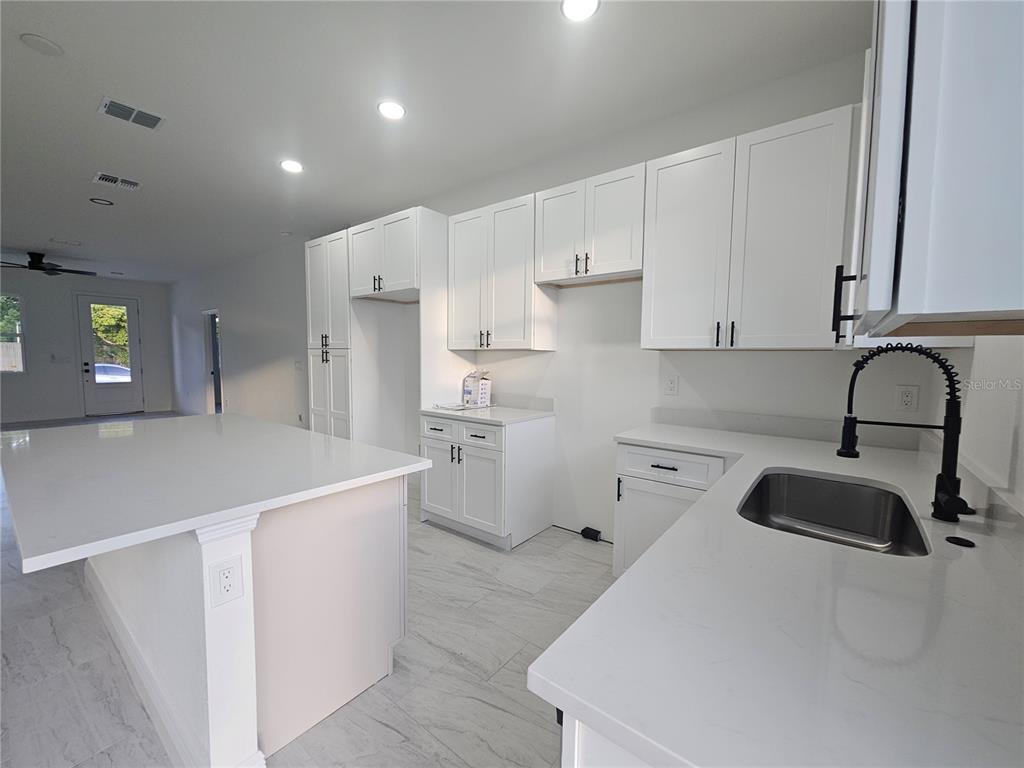 A modern kitchen features white cabinets, a large island, and light-colored tile flooring — 2068 DIXIE AVE, SANFORD, FL