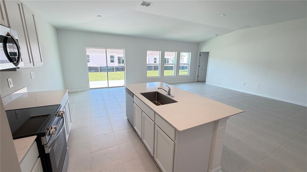 A modern kitchen with a central island, stainless steel appliances, and an open living area — 4585 GOLDEN KNIGHT BOULEVARD, KISSIMMEE, FL