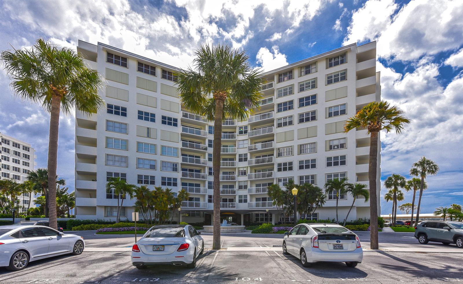 A multi-story white apartment building stands behind a parking lot with palm trees — 2600 N Flagler Drive # 803, West Palm Beach FL 33407, WEST PALM BEACH, FL