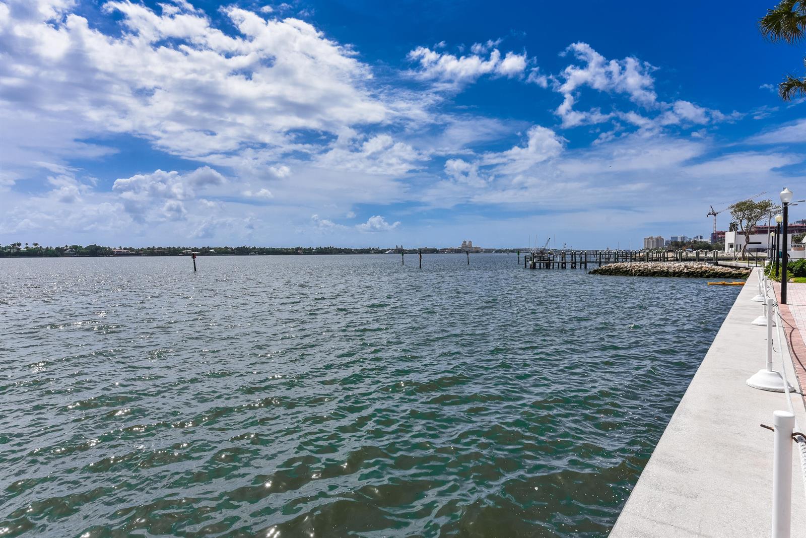 A concrete walkway runs along a body of water with a distant pier and skyline — 2600 N Flagler Drive # 803, West Palm Beach FL 33407, WEST PALM BEACH, FL
