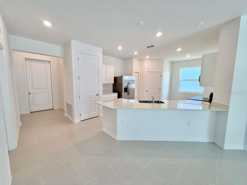 A modern kitchen features white cabinets, a quartz island, and light tile flooring — 3483 MUD CANYON DRIVE, DAVENPORT, FL