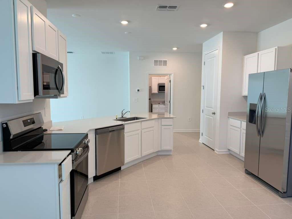 A modern kitchen features white cabinets, stainless steel appliances, and light-colored tile flooring — 3483 MUD CANYON DRIVE, DAVENPORT, FL