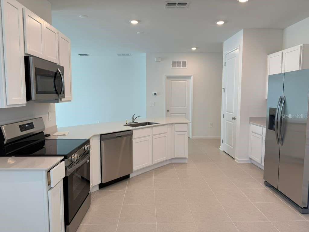 A modern kitchen features white cabinets, stainless steel appliances, and light-colored tile flooring — 3483 MUD CANYON DRIVE, DAVENPORT, FL