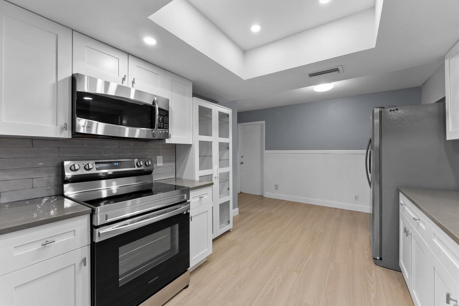 A kitchen features white cabinets, stainless steel appliances, gray countertops, and light wood-look flooring — 901 NW 49th Street, Deerfield Beach FL 33064, DEERFIELD BEACH, FL