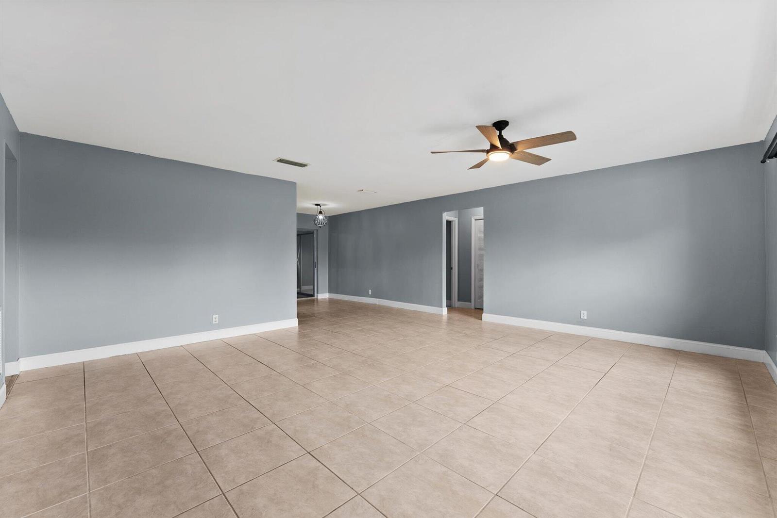 A spacious, empty room features gray walls, light-colored tile flooring, and a ceiling fan — 901 NW 49th Street, Deerfield Beach FL 33064, DEERFIELD BEACH, FL