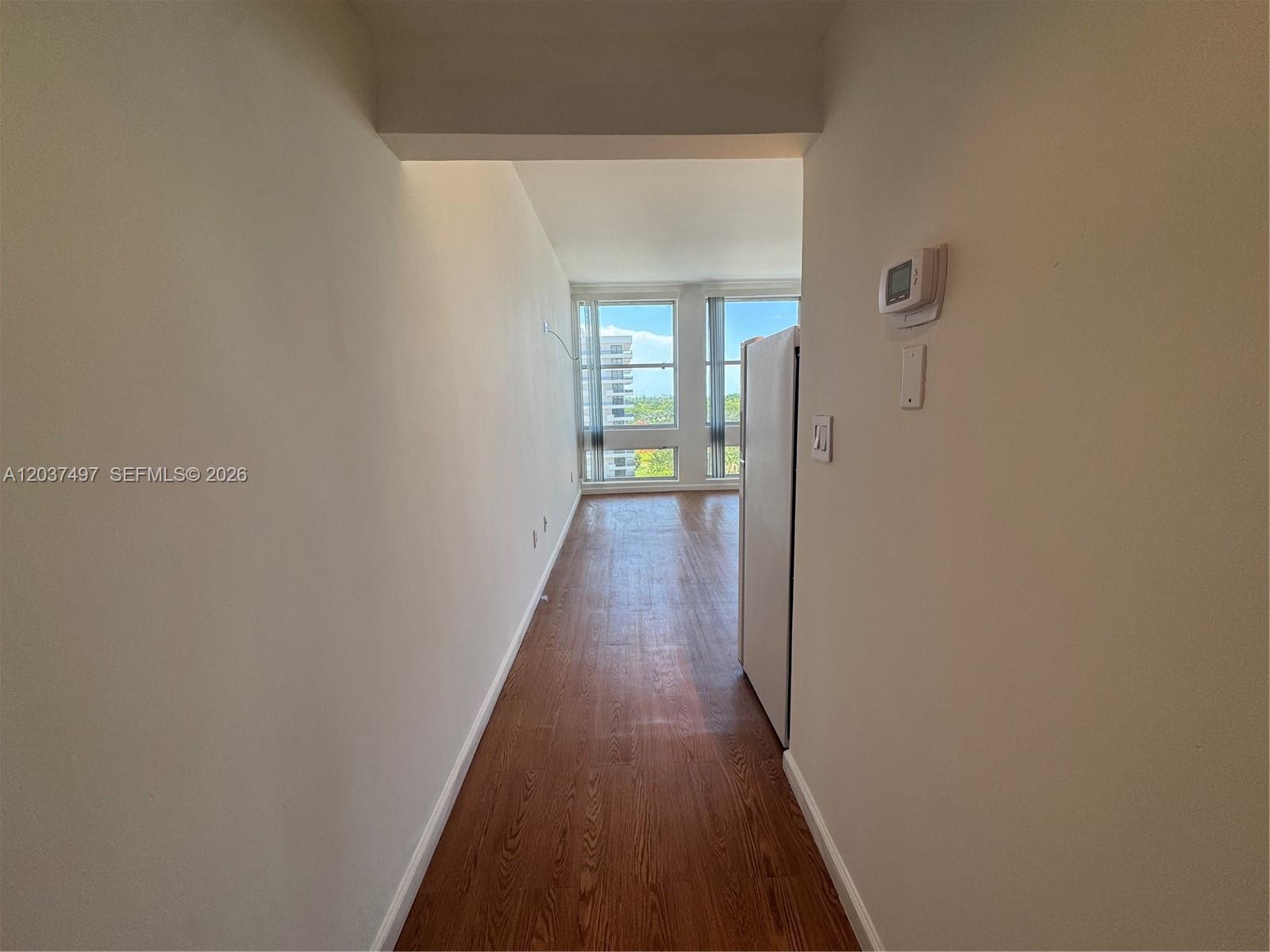 A narrow hallway with wood-look flooring leads toward a windowed room with city views — 700 Biltmore Way # 916, Coral Gables FL 33134, CORAL GABLES, FL