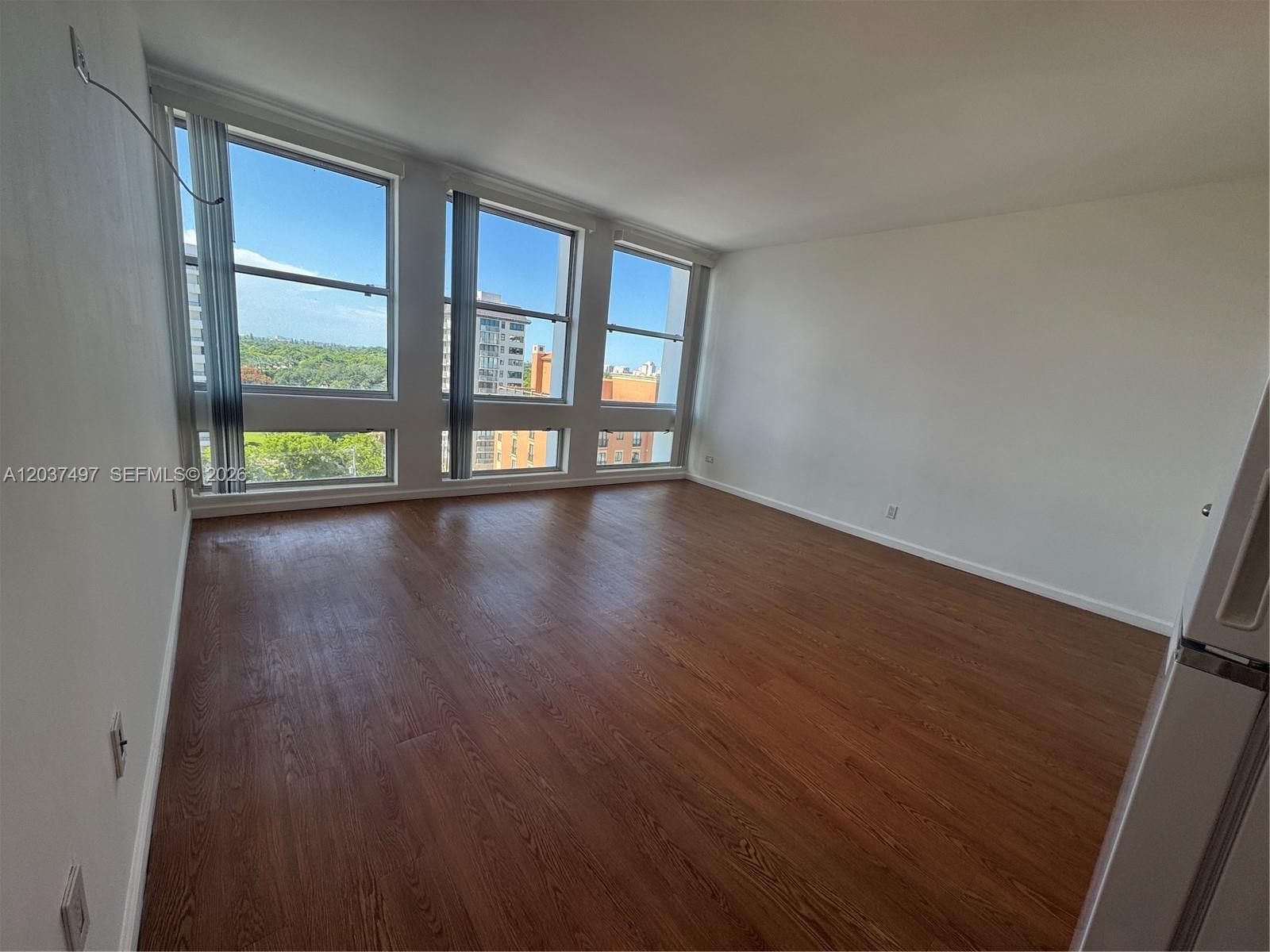 An empty room features wood-look flooring, white walls, and large windows with city views — 700 Biltmore Way # 916, Coral Gables FL 33134, CORAL GABLES, FL