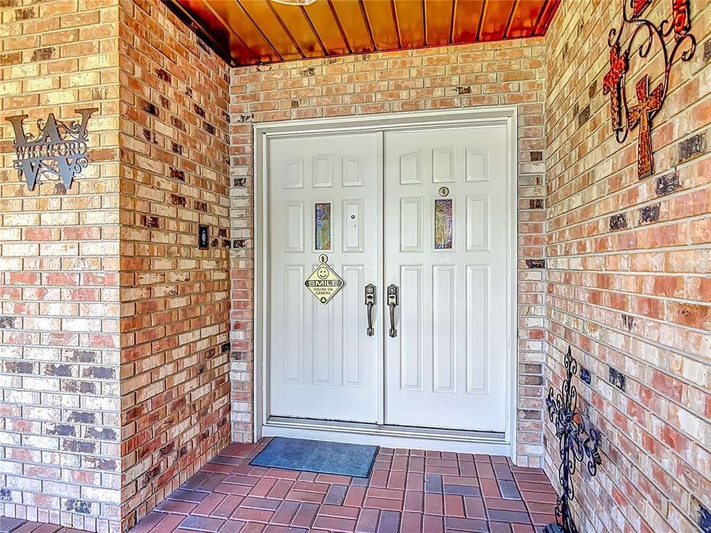 A brick entryway features a white double door with decorative glass inserts and a security sign — 17819 PALM STREET, UMATILLA, FL