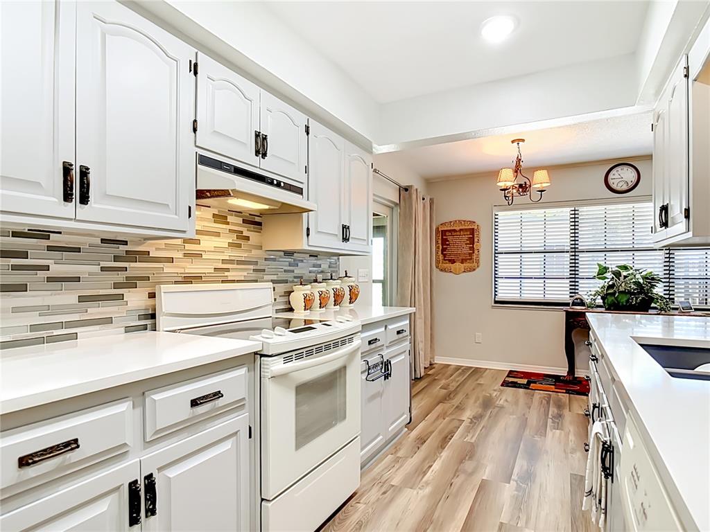 A kitchen features white cabinets, quartz countertops, a tiled backsplash, and light wood-look flooring — 17819 PALM STREET, UMATILLA, FL