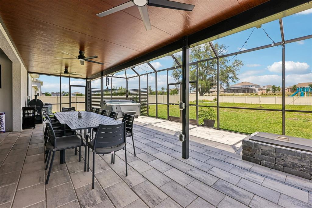 A covered patio features a dining set, hot tub, fire pit, and screened-in backyard view — 6100 SIERRA CROWN STREET, MOUNT DORA, FL