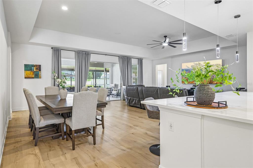 A dining area and kitchen island with light wood floors and a tray ceiling — 6100 SIERRA CROWN STREET, MOUNT DORA, FL