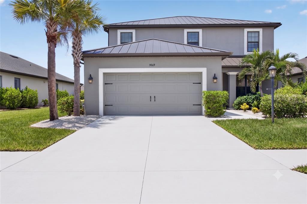 A two-story gray house features a metal roof, a two-car garage, and palm trees — 9069 LUNA LANE, SARASOTA, FL