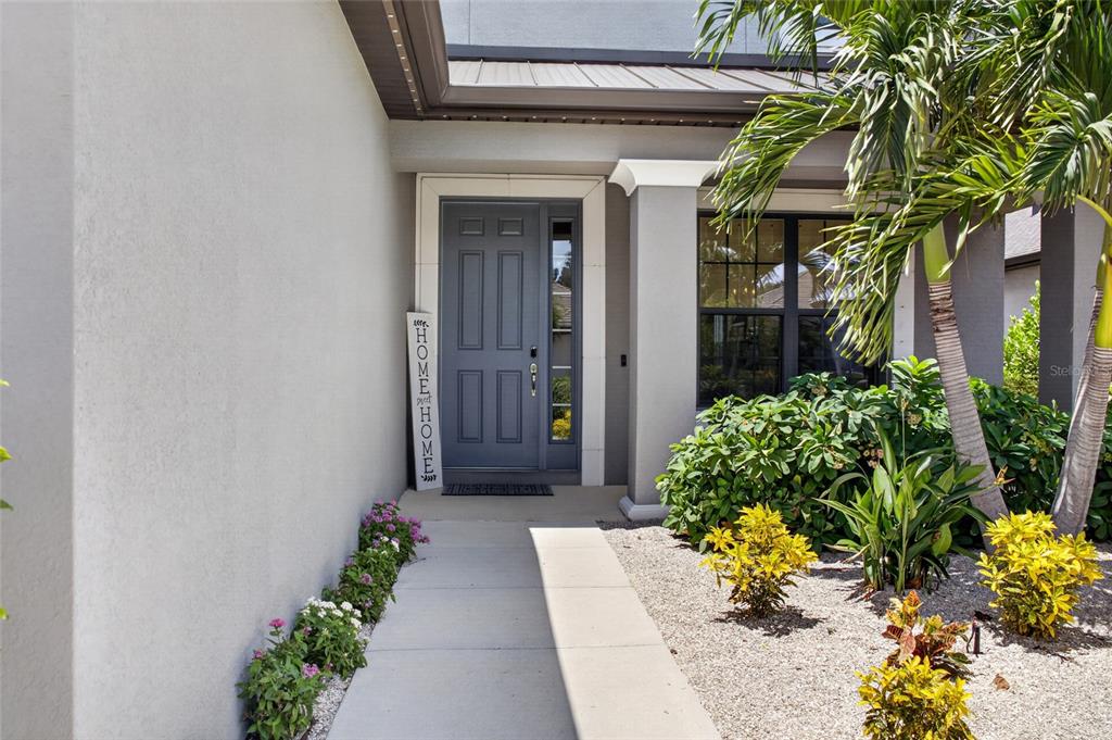 A concrete walkway leads to a gray front door with a side window and landscaping — 9069 LUNA LANE, SARASOTA, FL