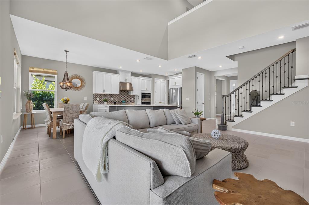 A bright open-concept living room and kitchen featuring light gray walls, tile floors, and stairs — 9069 LUNA LANE, SARASOTA, FL