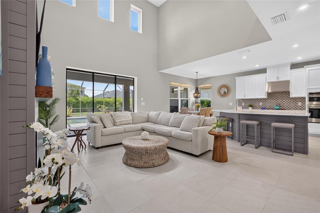 An open-concept living room and kitchen with high ceilings, tile floors, and a sectional sofa — 9069 LUNA LANE, SARASOTA, FL