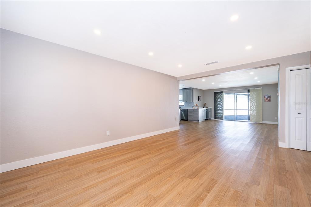 A spacious room with light wood-look flooring and recessed lighting leads to a kitchen area — 4522 FETROW DRIVE, ORLANDO, FL