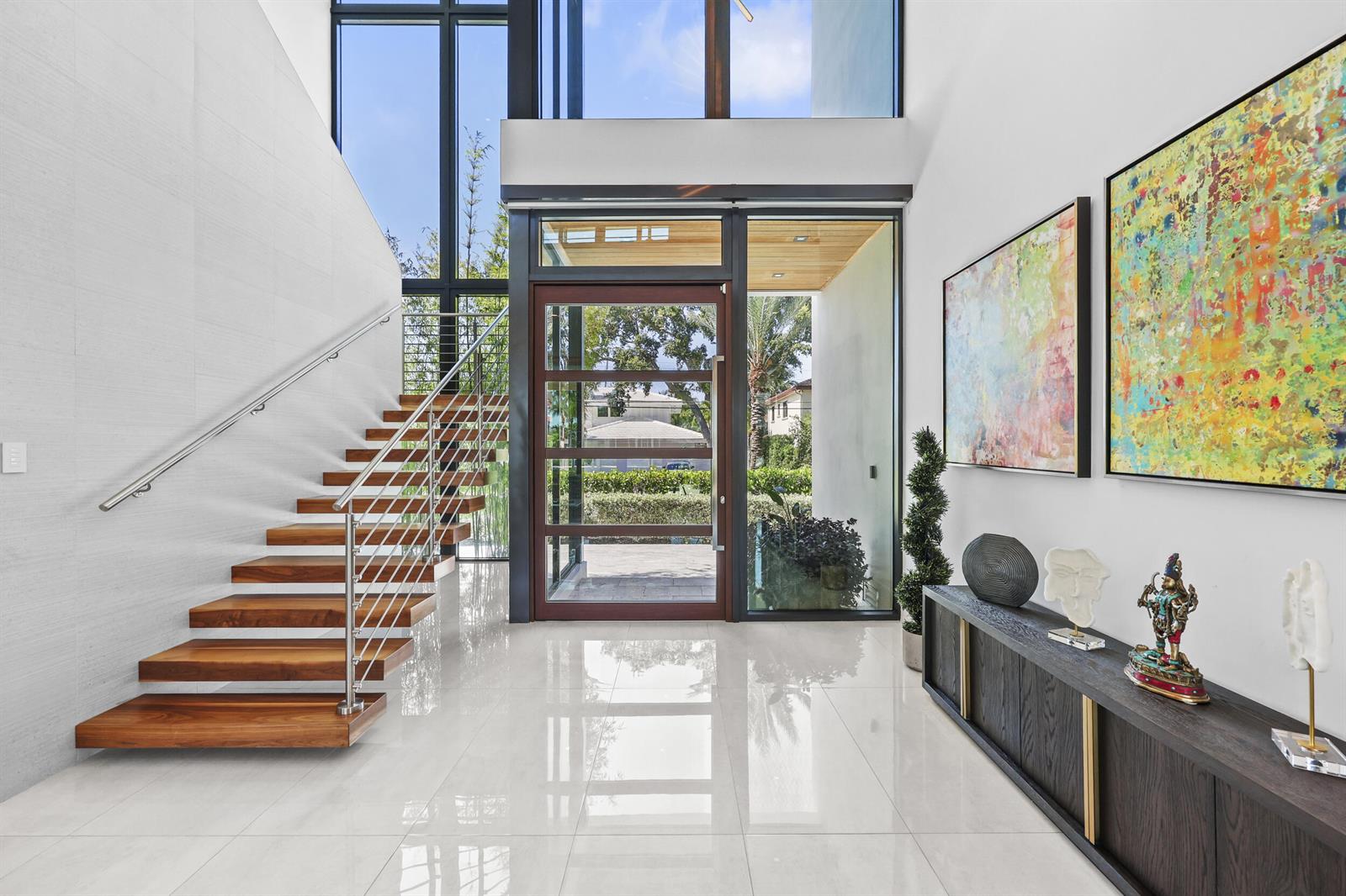 A modern entryway features a floating wooden staircase, large glass windows, and a console table — 2863 NE 27th Street, Fort Lauderdale FL 33306, FORT LAUDERDALE, FL