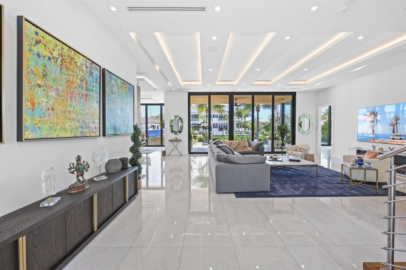 A bright, open-concept living room features white tile floors, a gray sectional, and large glass doors — 2863 NE 27th Street, Fort Lauderdale FL 33306, FORT LAUDERDALE, FL