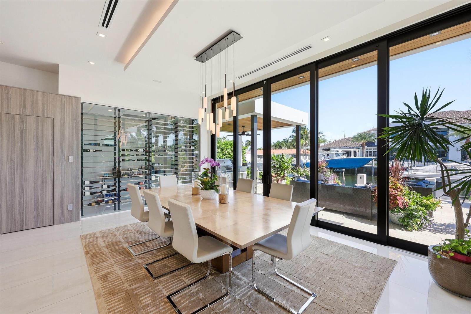 A modern dining room features a large table, glass wine cellar, and floor-to-ceiling sliding doors — 2863 NE 27th Street, Fort Lauderdale FL 33306, FORT LAUDERDALE, FL